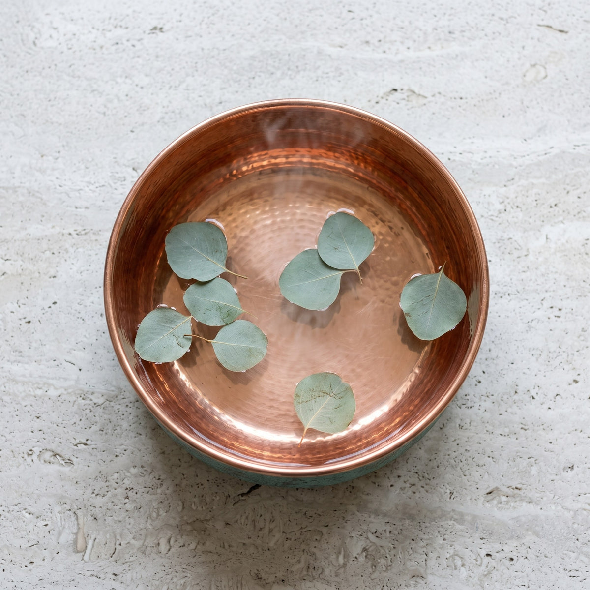 Copper foot soaking bowl filled with water and eucalyptus leaves seen from above