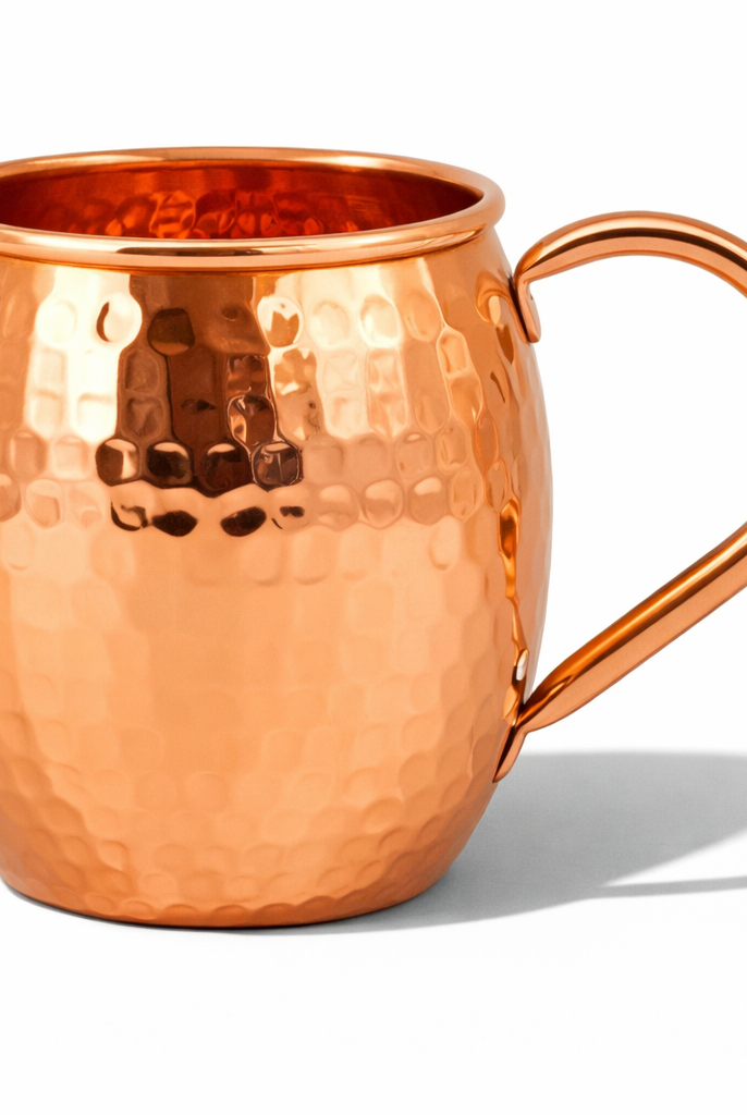 A beautiful hand-hammered shiny copper mug displayed on a table.
