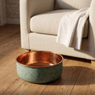 Copper pedicure bowl on an oak floor beside a linen armchair and folded towel