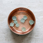 Copper foot soaking bowl filled with water and eucalyptus leaves seen from above