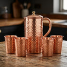 Hand hammered copper jug and four matching copper glasses from the 1.5L set, on a timber table